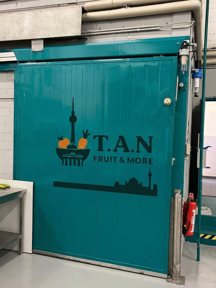 Türkisfarbene Kühlraumtür mit dem T.A.N. Fruit & More Logo